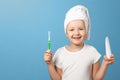 Closeup portrait of a little girl on a blue background. A child with a white towel on his head holding a toothbrush and toothpaste Royalty Free Stock Photo