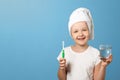 Closeup portrait of a little girl on a blue background. A child with a white towel on his head holds a toothbrush and a glass of Royalty Free Stock Photo