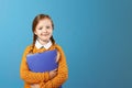 Closeup portrait of a little girl schoolgirl. Pretty child in a yellow sweater holds a purple folder for papers on a blue Royalty Free Stock Photo