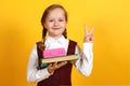 Closeup portrait of a little girl schoolgirl on a yellow background. The child has a lunch box and a book in his hand. Royalty Free Stock Photo