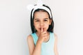 Closeup portrait of little girl wearing blue dress, white bow showng silence gesture isolated over white studio wall. Cute child Royalty Free Stock Photo