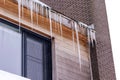 A closeup portrait of long icicles hanging from a roof gutter above a window during winter after a blizzard. The ice is dangerous Royalty Free Stock Photo