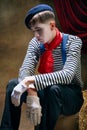 Closeup portrait of male mime artist expressing sadness and loneliness over dark retro circus backstage background