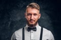 Closeup portrait of a man with stylish beard and hair in shirt with bow tie and suspenders. Studio photo against dark