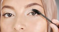 Closeup portrait of muslim woman applying mascara makeup to eyelashes. Headshot of stunning arab model doing her beauty Royalty Free Stock Photo