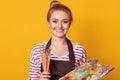 Closeup portrait of positive adorable cute painter wearing stripped sweatshirt, brown apron, accessories, holding dirty palette