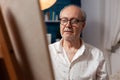 Closeup portrait of retired man artist looking inspired at canvas on easel while drawing using pencil Royalty Free Stock Photo