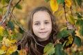 Closeup portrait of a romantic charming little girl in fall yellow leaves. Smiling child girl with big eyes looking in camera.