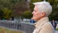 Closeup portrait 65s happy smiling mature lady in casual clothes standing posing outdoors turns head looking aside. Calm Royalty Free Stock Photo