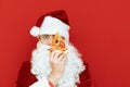 Closeup portrait of Santa Claus holding a slice of pizza in front of his eye and looking into the camera with a serious face