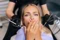 Closeup portrait of scared blonde young woman closing mouth by fear in dental clinic, afraid of treatment. Cropped shot Royalty Free Stock Photo