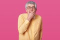 Closeup portrait of scared elderly man with short haistyle. Senior with opened mouth, keeps hand up to face, looks at camera with Royalty Free Stock Photo