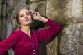 Closeup portrait of sensual cute girl with tiara posing with lifted hand near old stony wall outdoor