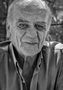 Closeup portrait of a serious old greek retired male who smokes a cigarette with a smile, in black and white