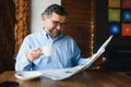 Closeup portrait of serious senior handsome man reading newspaper, having coffee break and sitting at table. Royalty Free Stock Photo