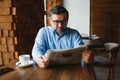 Closeup portrait of serious senior handsome man reading newspaper, having coffee break and sitting at table. Royalty Free Stock Photo