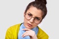 Closeup portrait of serious young woman wearing casual outfit, round transparent eyewear, being doubtful, looking to the camera.