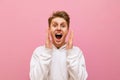 Closeup portrait of shocked guy in white hoodie on pink background looking into camera with mouth open and shouting with joy. Royalty Free Stock Photo