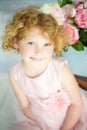 Close up portrait of small 5 years old smiling blonde curly girl in beautiful princess dress with pink flowers on background. Royalty Free Stock Photo