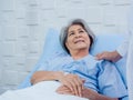 Closeup portrait of smiling Asian elderly, senior woman patient in light blue dress lying on bed. Royalty Free Stock Photo