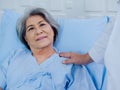 Closeup portrait of smiling Asian elderly, senior woman patient in light blue dress lying on bed. Royalty Free Stock Photo