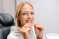 Closeup portrait of smiling blonde female patient holding invisible braces aligner sitting on chair in dentistry clinic Royalty Free Stock Photo