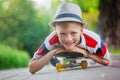 Closeup portrait smiling boy in hat lying on skateboard in summer