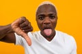 Closeup portrait of a smiling handsome black blond african man with thumb down on orange background Royalty Free Stock Photo