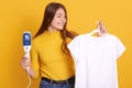 Closeup portrait of smiling woman wearing yellow casual shirt, lady choosing outfit for dating, holding hangers with t shirt in Royalty Free Stock Photo