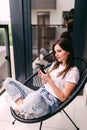 Closeup portrait of smiling young beautiful woman talking on smartphone and sitting on chair on balcony at home Royalty Free Stock Photo
