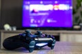 A closeup portrait of a sony playstation 4 video game controller in front of a television with the playstation home menu displayed Royalty Free Stock Photo