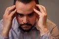 Closeup portrait of a stressed middle-aged man in grey shirt sitting indoor with sad face and thinking holding head in hands