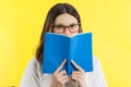 Closeup portrait teenage girl with eye glasses looking over a book, yellow background Royalty Free Stock Photo
