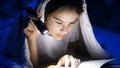 Closeup portrait of teenage girl lying under blanket and reading book Royalty Free Stock Photo