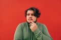 Closeup portrait of a thoughtful bearded hispanic man standing on a red background, expressing a thinking gesture, touching his Royalty Free Stock Photo