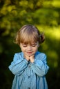 Closeup portrait tiny girl in blue jeans dress, with closed eyes, smiling to camera, on sunny green meadow. Summer time, Sunshine Royalty Free Stock Photo