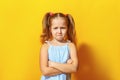 Closeup portrait of upset little girl on yellow background. The child crossed his arms and pouted his lips