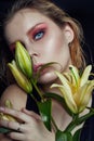 Closeup portrait of woman with flowers lilies in his hands, bright contrasting makeup on the girl`s face. Wet hair and clean