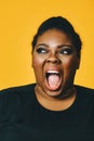 closeup portrait of a young adult african american woman in shock with mouth open screaming on yellow background