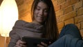 Closeup portrait of young attractive caucasian female using the tablet while resting laidback on the sofa and smiling