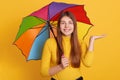 Closeup portrait of young beautiful Caucasian woman holding colorful umbrella isolated over yellow background. Lady spreading palm Royalty Free Stock Photo