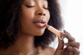 Closeup portrait of young black lady applying lipstick with closed eyes, taking care of her appearance indoors Royalty Free Stock Photo