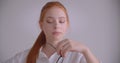 Closeup portrait of young cute caucasian redhead female looking at camera holding her glasses with thoughtfulness