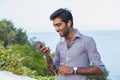 Closeup portrait, young happy handsome man standing, checking his cellphone, listening to music, isolated on seaside summer Royalty Free Stock Photo