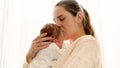 Closeup portrait of young loving mother kissing her little newborn baby at window Royalty Free Stock Photo