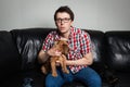 Closeup portrait, young man in the red shirt, sitting on black leather couch with two dogs, watching TV, holding remote, surprised Royalty Free Stock Photo