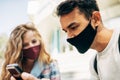 Closeup portrait of a young man and a woman sitting outside looking to the smartphone. Two young students in protective face masks Royalty Free Stock Photo