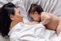 Closeup portrait of young mother breastfeeding her little daughter in bedroom, gray background. Baby suckle milk and get