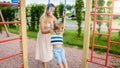 Closeup portrait of young mother helping and holding her little son hanging and swinging on sportrs rings at palyground Royalty Free Stock Photo