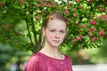 Closeup portrait of young natural beautiful redhead woman in fuchsia blouse posing against blossoming tree with blurred green foli Royalty Free Stock Photo